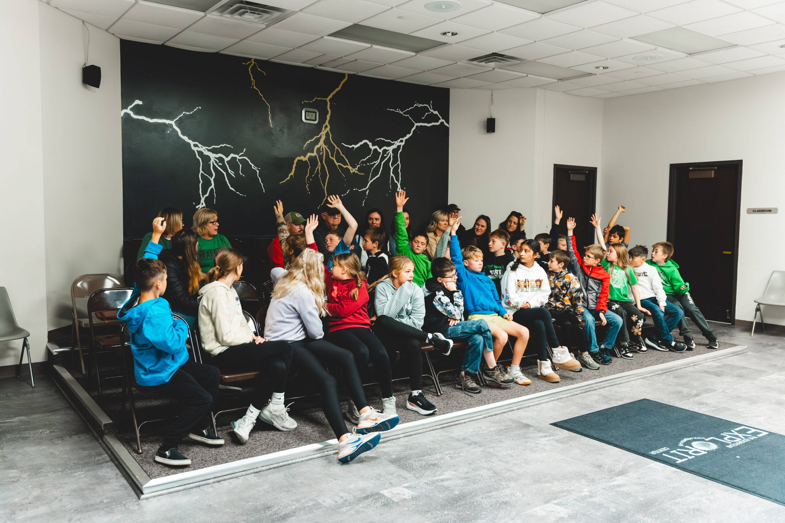 a group of students sitting in a room at the Edgerton Center raising their hands